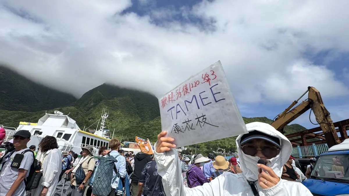 夥伴在碼頭高舉手寫的 TAMEE 紙牌,背後是船隻與山巒
