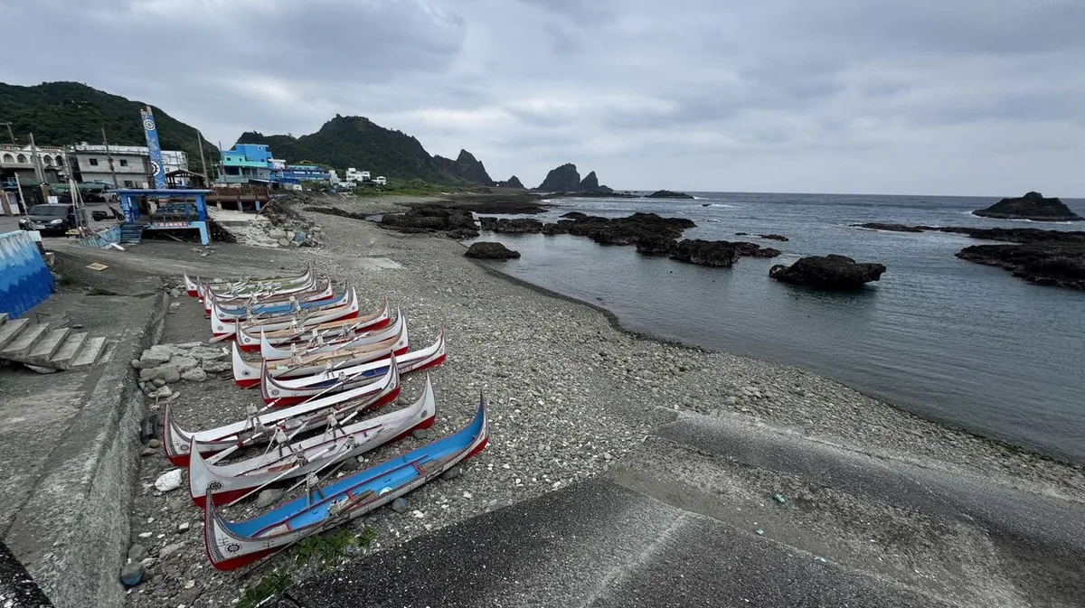 海灘上並排停放的拼板舟,後方是海岬與聚落