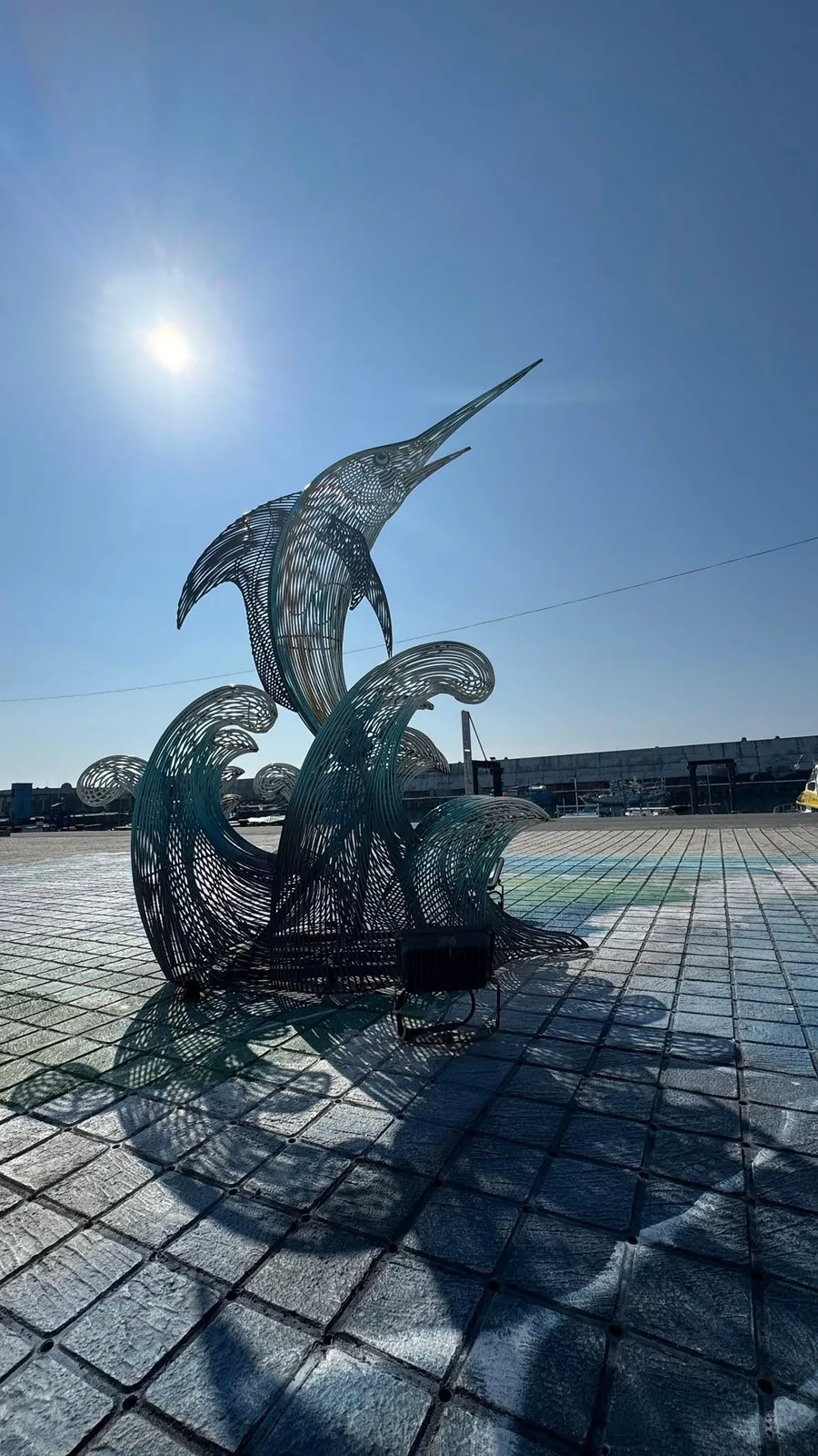 成功漁港廣場上的鏤空金屬旗魚雕塑,旗魚躍出浪花,背景是藍天與漁港防波堤