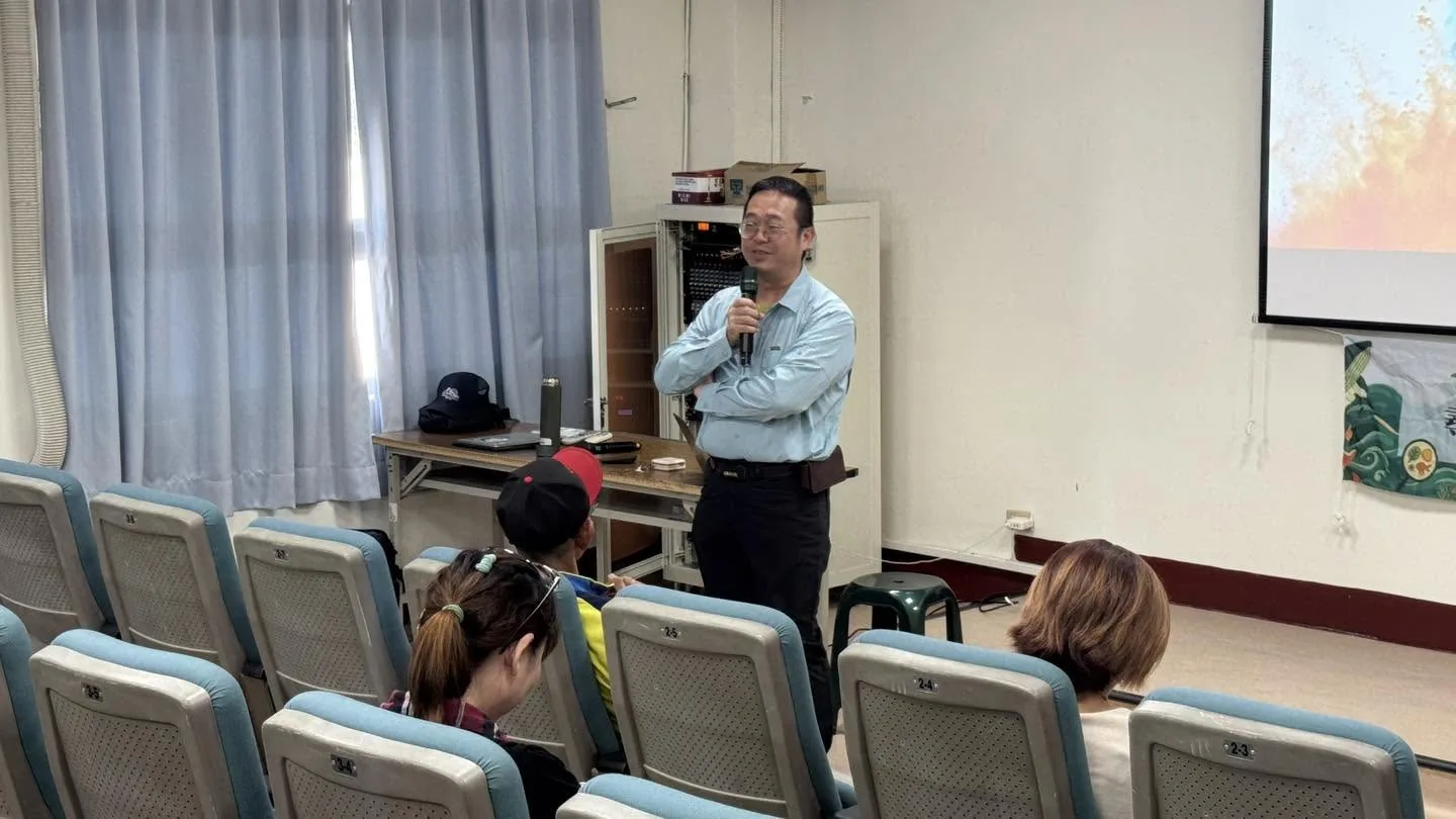 講師穿淺藍襯衫拿著麥克風,在簡報室前方對學員講課