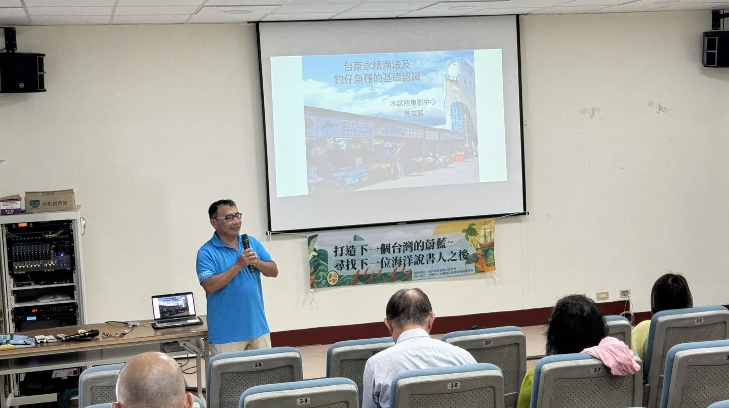 吳瑞賢在投影幕前講課,投影片標題是「台東永續漁法及釣仔魚種的基礎認識」,下方掛著活動布條