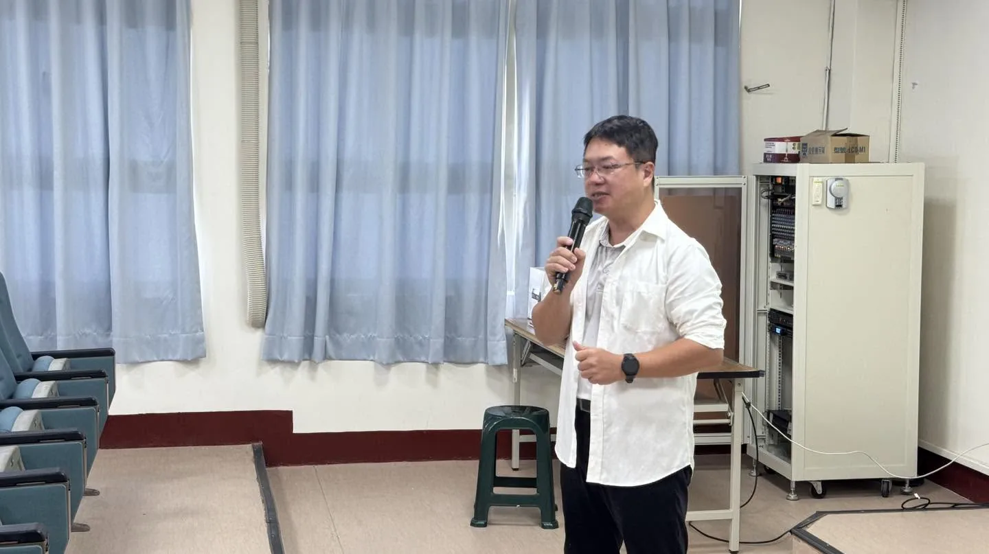 穿白襯衫的講師站在簡報室前方拿著麥克風分享