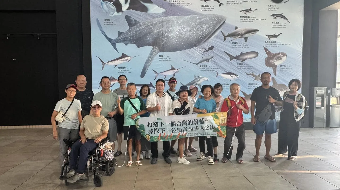 學員在水族生態研究館的巨幅海洋生物壁畫前,拉著活動布條合影