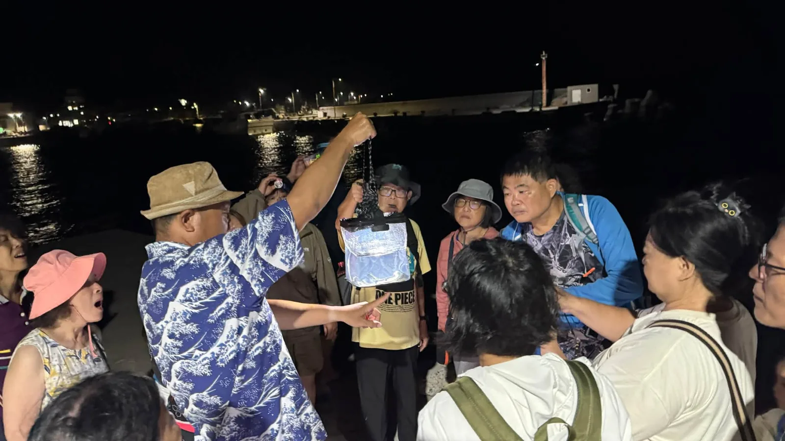 夜探漁港,講師舉著圖卡向圍成一圈的學員解說