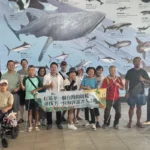 說書人台東場學員在水族生態研究館的巨幅海洋生物壁畫前,拉著「打造下一個台灣的蔚藍」布條合影
